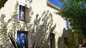 Un edificio con fachada color crema, una ventana con persiana azul y una puerta con un ventanal pequeño.