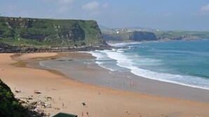 A coastal beach with a sandy shore, cliffs, and a clear sky. - Hotel Marfrei (Suances)