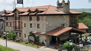 A stone building with a tiled roof, a sign reading "HOTEL," and a covered outdoor seating area. - Hotel Marfrei (Suances)