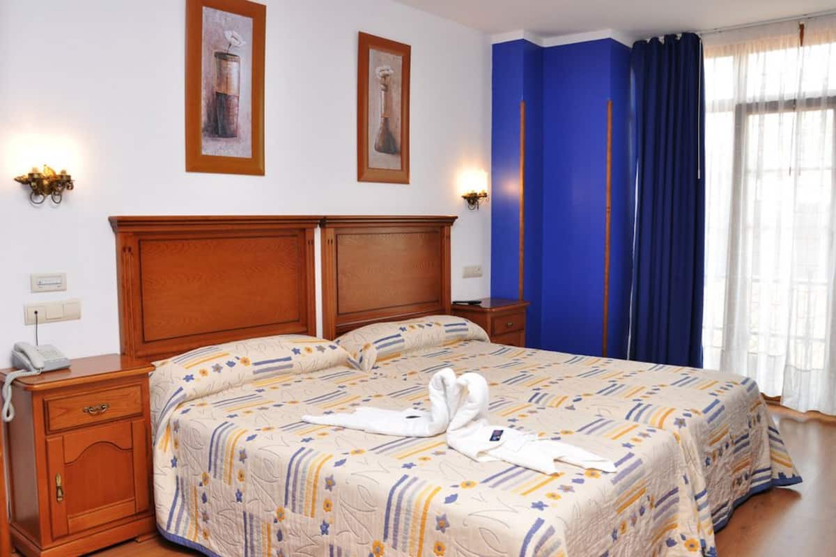 A hotel room with a wooden bed, a telephone on the nightstand, and two wall-mounted lamps.