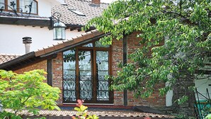 A traditional brick house with a sloped roof, a large window with decorative iron bars, and lush greenery around the property. - Hotel Marfrei (Suances)