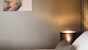 A neatly made bed with white and gray bedding, a wall-mounted picture of a deer, and a patterned wall lamp. - Hotel Waltikka (Valkeakoski)