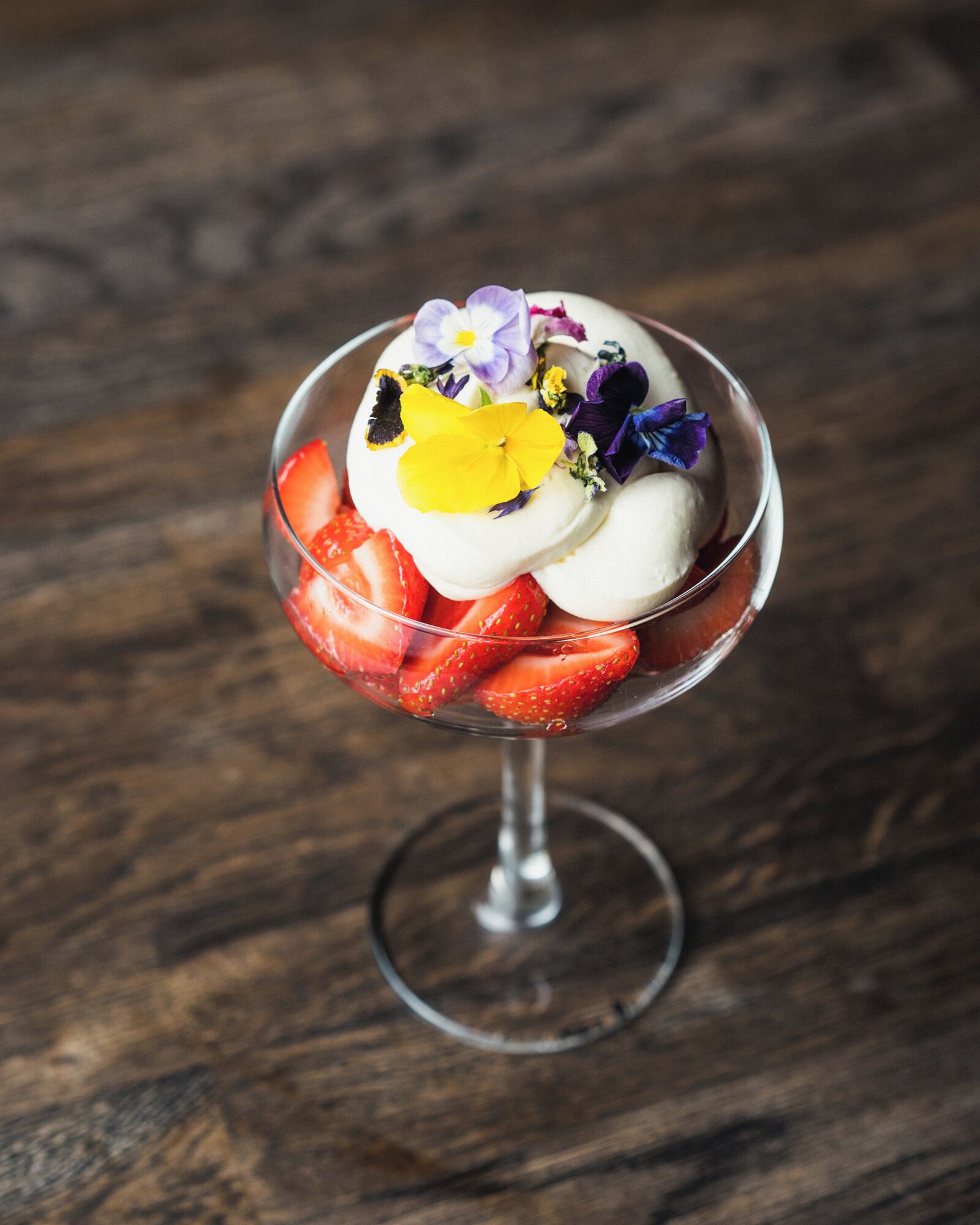 Ein Dessert in einer Glaskugel mit Erdbeeren und Blüten.