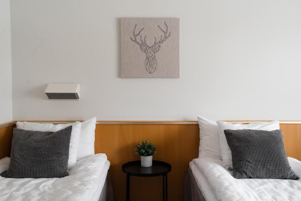 Een hotelkamer met twee bedden, een klein nachtkastje met een plant en een wanddecoratie van een hertenhoofd.