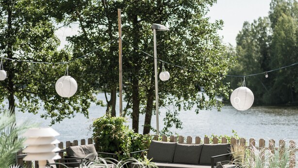 An outdoor seating area with a view of a lake, featuring wooden tables, chairs, and a sofa. - Hotel Waltikka (Valkeakoski)