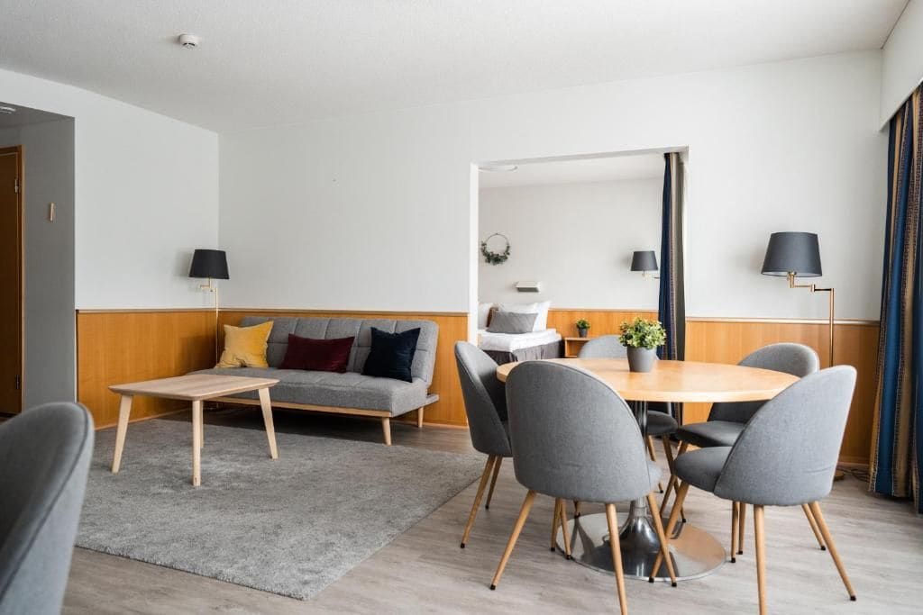 A modern living room with a sofa, a coffee table, and a dining area with chairs and a table.