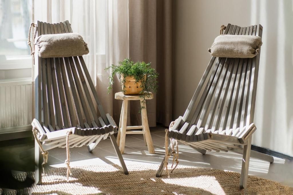 Deux fauteuils confortables avec coussins, un petit tabouret en bois surmonté d’une plante et un tapis tissé posé sur un sol carrelé.