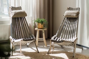 Two lounge chairs with cushions, a small wooden stool with a plant, and a woven rug on a tiled floor.