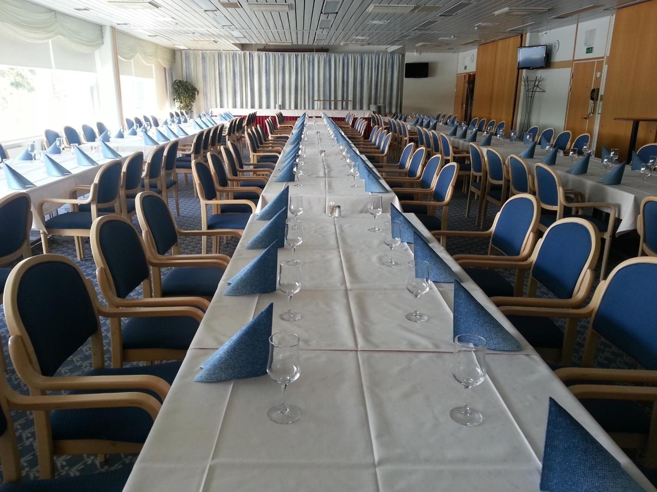 Un salón de conferencias con una larga mesa, sillas azules y copas de vino.