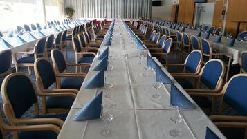 Un salón de conferencias con una larga mesa, sillas azules y copas de vino.