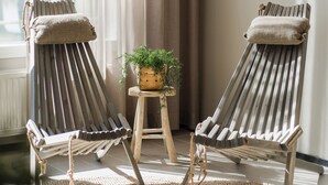 Two wooden lounge chairs with cushions, a small wooden stool with a plant, and a woven rug on a wooden floor. - Hotel Waltikka (Valkeakoski)
