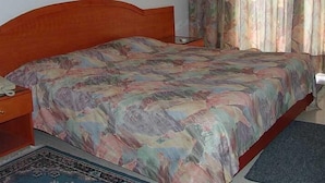 A bed with a patterned bedspread, a bedside table with a lamp, and a wooden nightstand. - Hotel Monte bello (Ajaltoun)