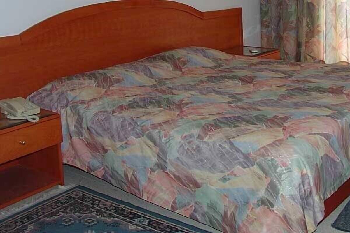 A bed with a patterned bedspread, a bedside table with a lamp, and a wooden nightstand.