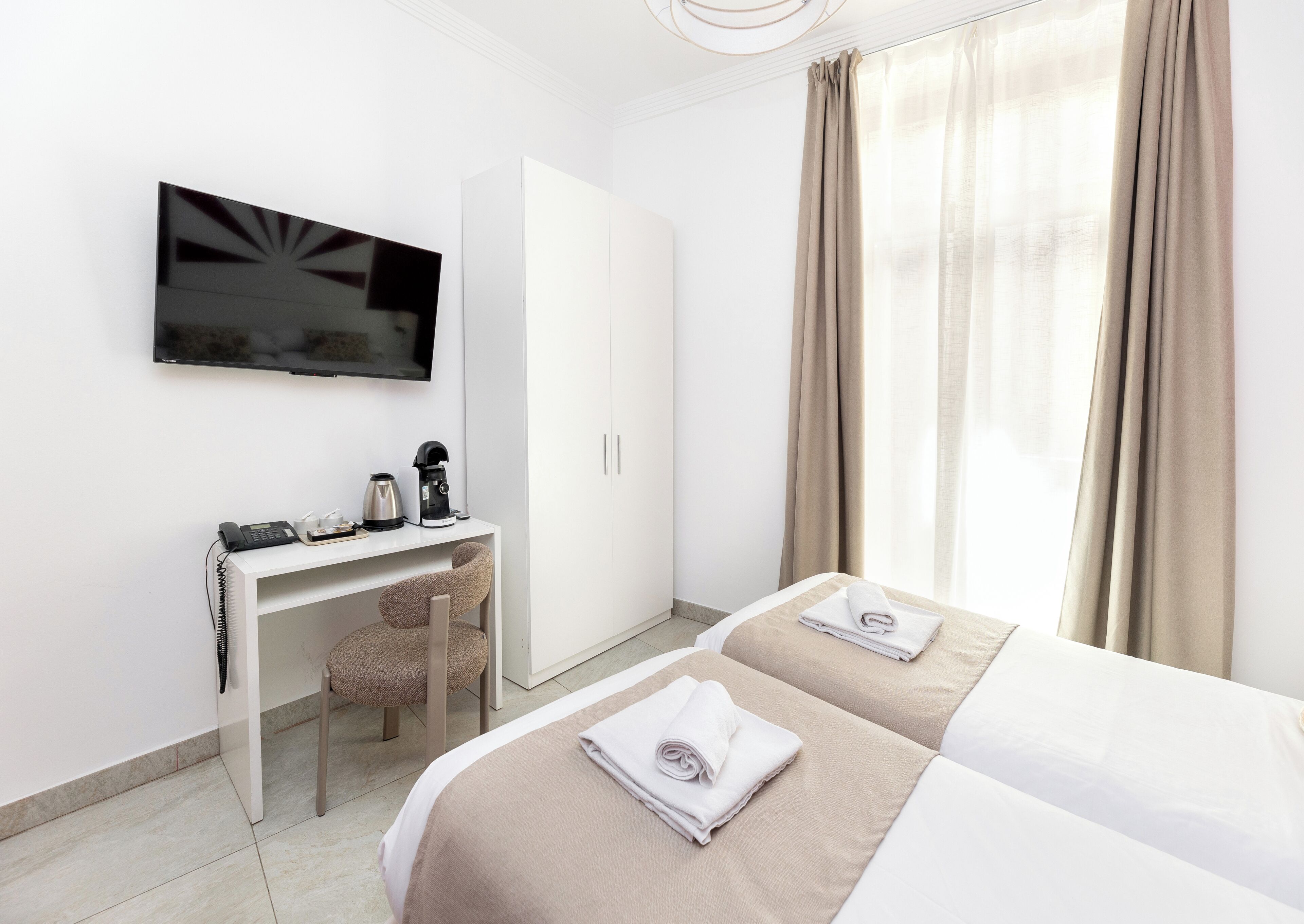 Habitació d'hotel amb un llit, una taula de nit amb una cafetera, un televisor i una cadira.