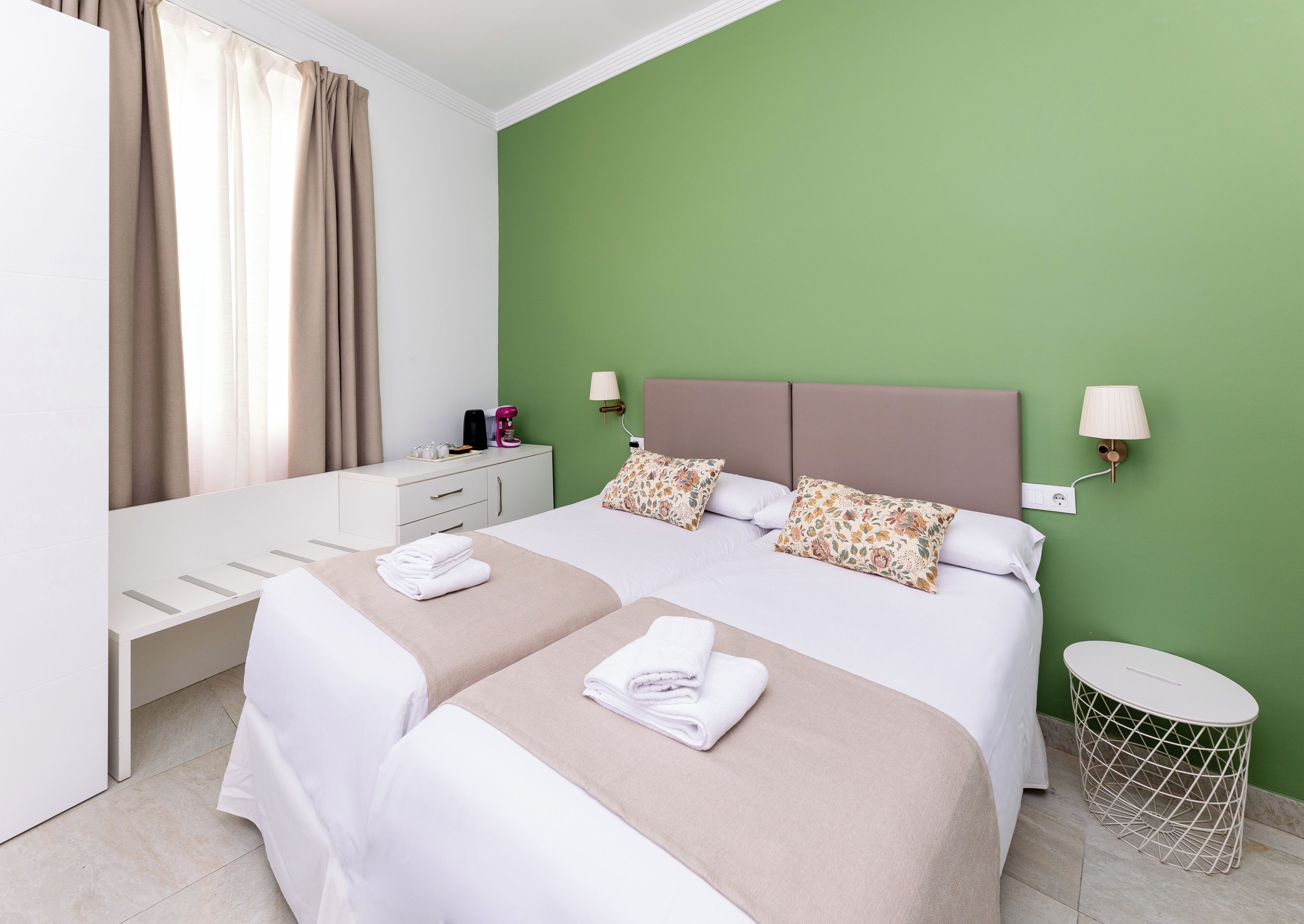 Una habitación de hotel con cama, mesitas de noche, lámpara, una pequeña mesa y un cubo de basura.