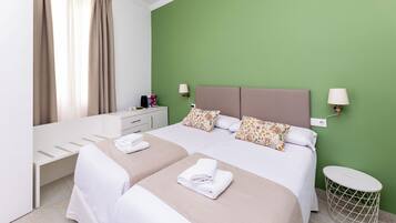 Una habitación de hotel con cama, mesitas de noche, lámpara, una pequeña mesa y un cubo de basura.