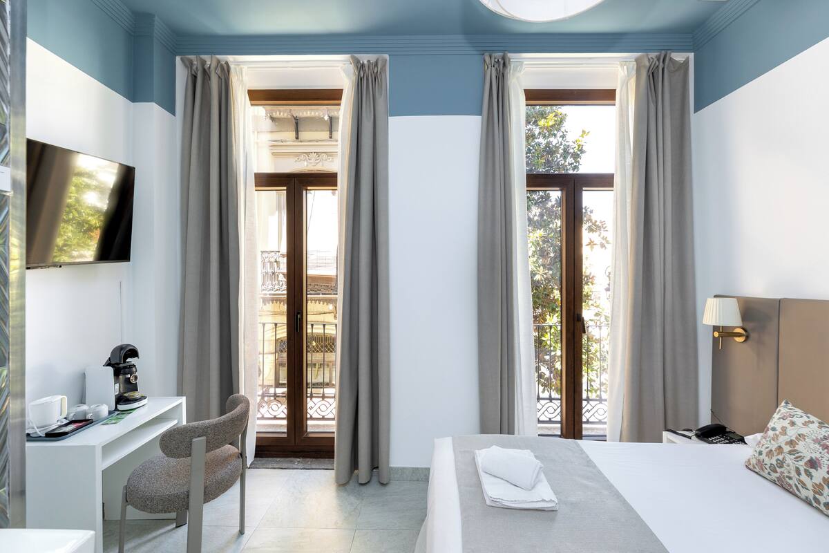 A hotel room with a bed, desk, chair, TV, and a balcony view.