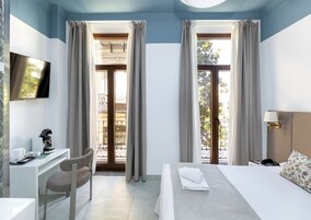 Habitación de hotel con cama, escritorio, silla, televisor y vista al balcón.