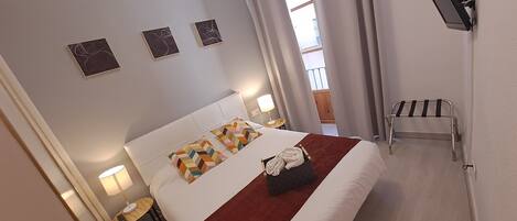 Quarto de hotel com cama, mesa de cabeceira com abajur, pequena mesa com abajur, porta-toalhas e vista para a varanda.