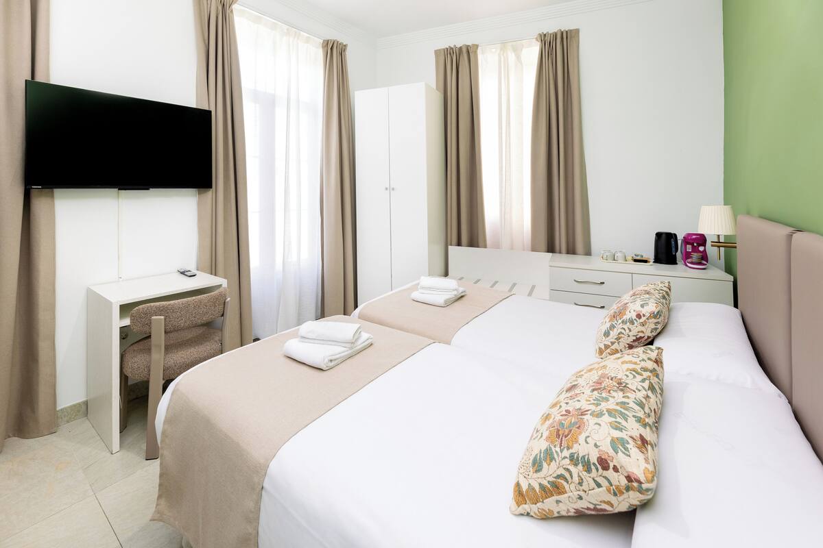 A hotel room with a bed, a desk, a television, and a green wall.