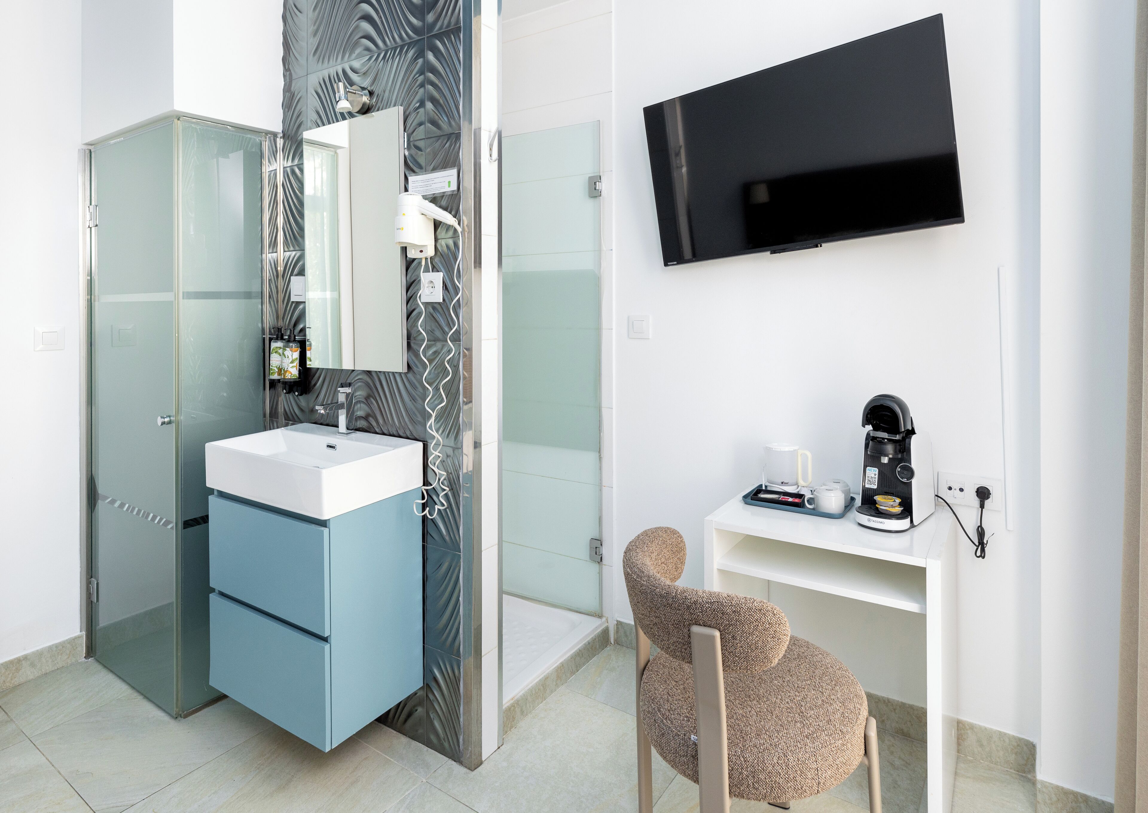 A modern bathroom with a glass shower enclosure, a white sink, a mirror, a towel rack, a toilet, and a television mounted on the wall.