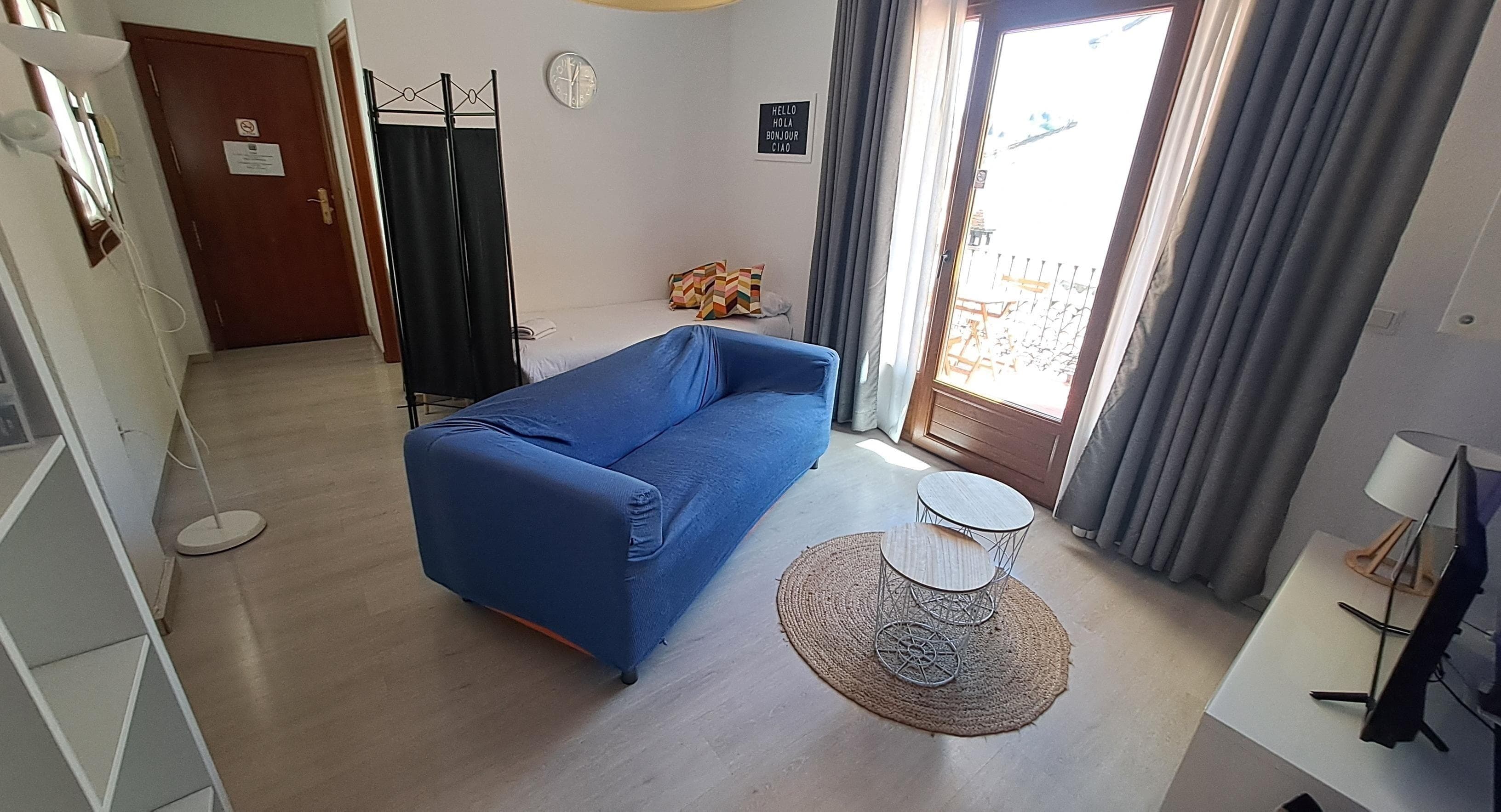 A room with a blue sofa, a small round table, a door with a sign, and a window with curtains.