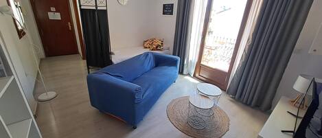 A room with a blue sofa, a small round table, a door with a sign, and a window with curtains.