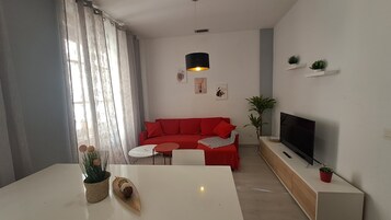 Una sala de estar moderna con un sofá rojo, una mesa de centro blanca, un televisor y una planta pequeña sobre un mueble de madera.