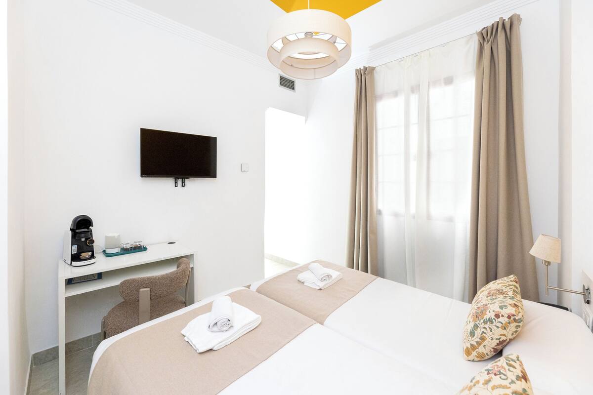 A hotel room with a bed, a desk with a coffee maker, a TV, and a window with curtains.