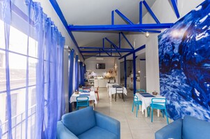 Un restaurante con decoración azul y blanca, que incluye mesas, sillas, una zona de cocina y un gran mural azul.
