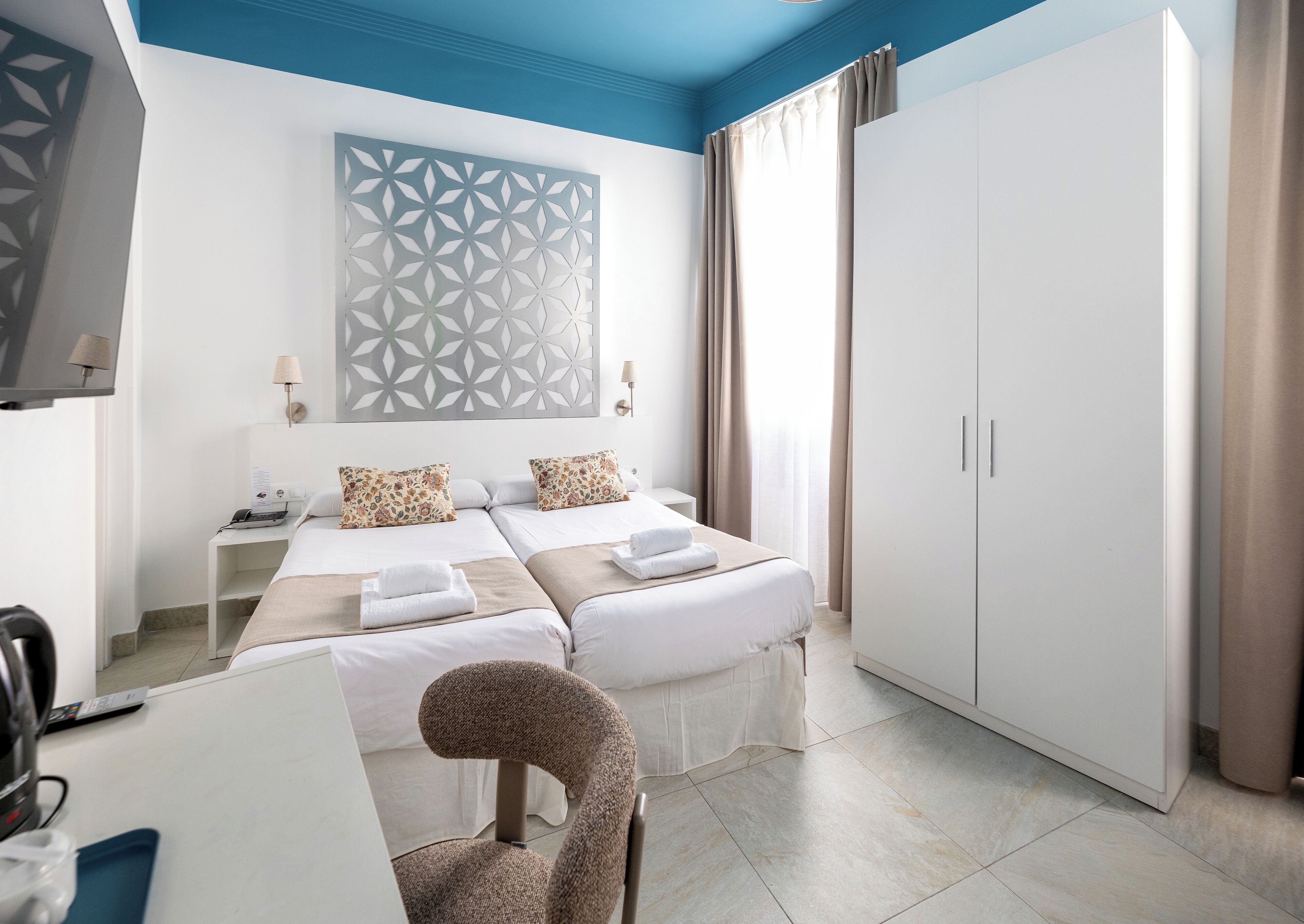 A hotel room with a bed, a desk, a chair, a wardrobe, and a decorative wall panel.