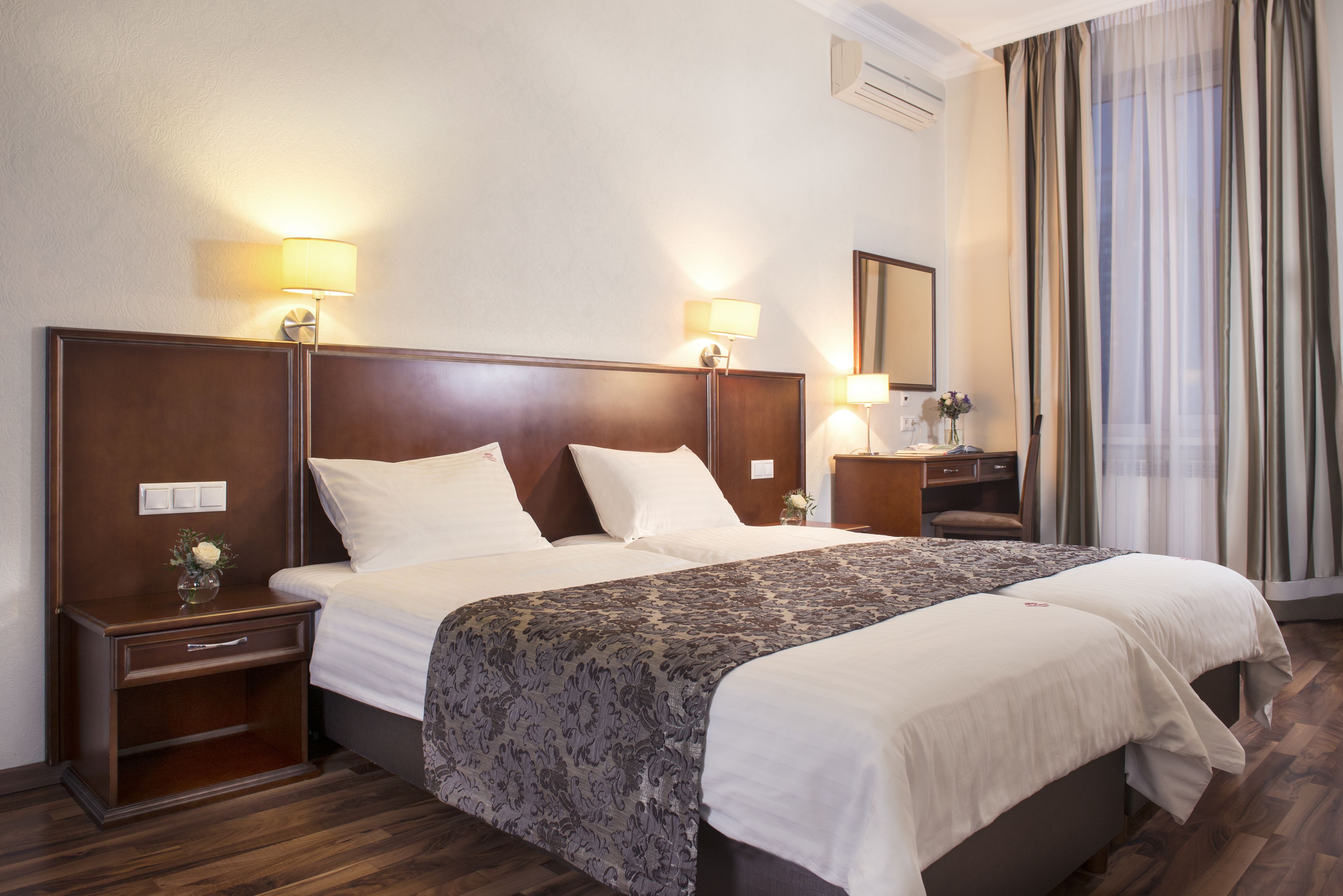 A hotel room with a large bed, two bedside tables with lamps, a desk, and a mirror.