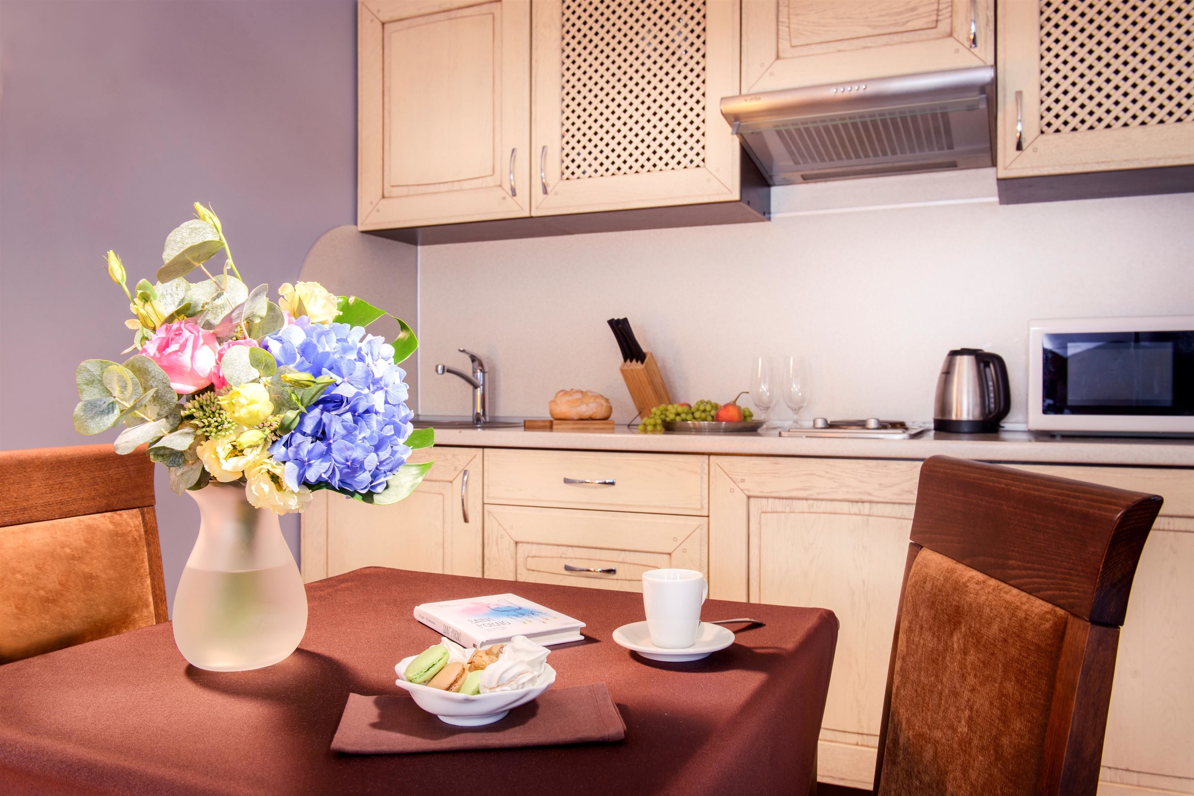 Un comedor con una mesa dispuesta para dos personas, un jarrón de flores y una bandeja de desayuno con croissants y fruta.