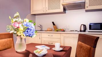 A dining area with a table set for two, a vase of flowers, and a breakfast spread including croissants and fruit.