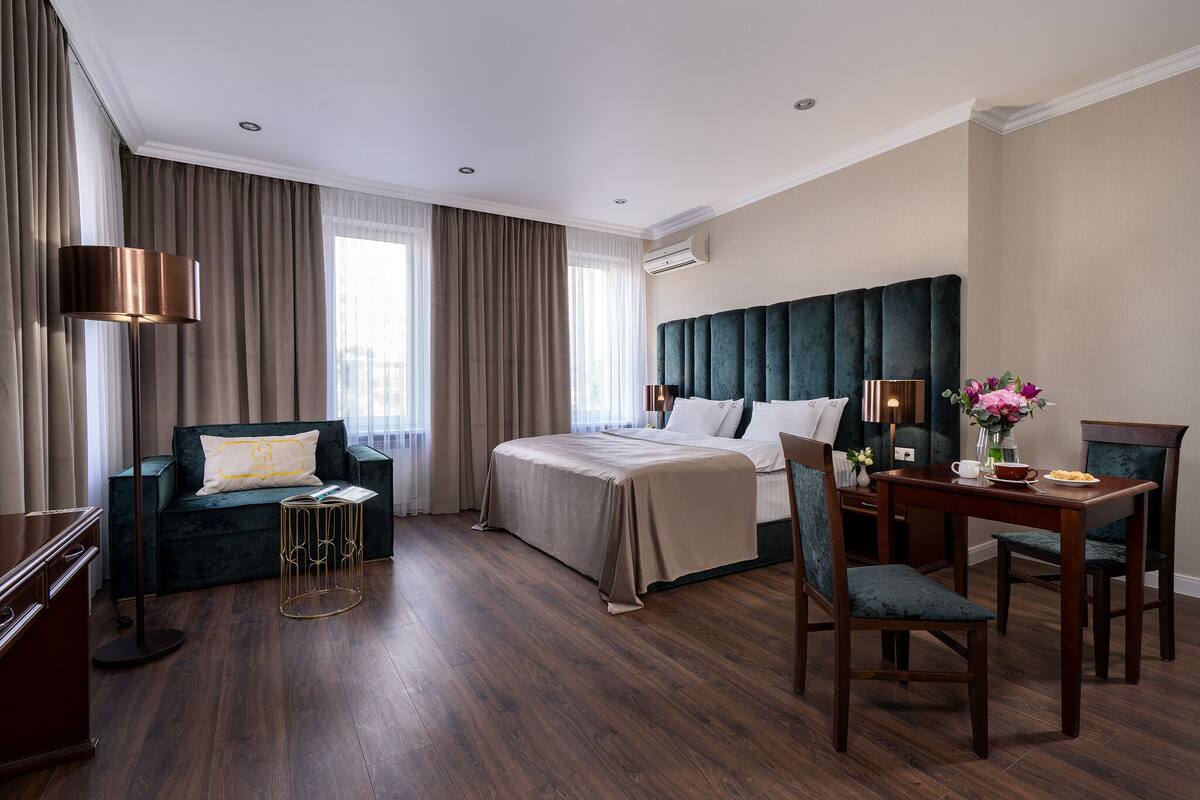 A hotel room with a bed, a sofa, a dining table, and a desk.