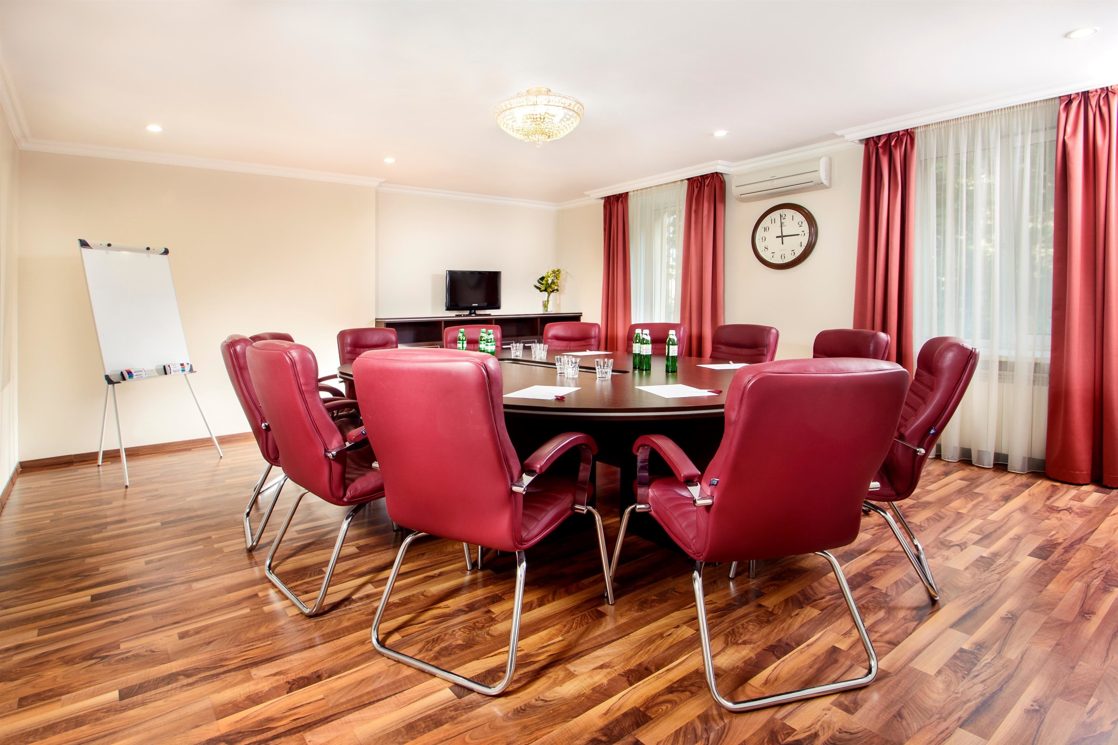 A conference room with a round table, red chairs, a whiteboard, a television, and a clock on the wall.