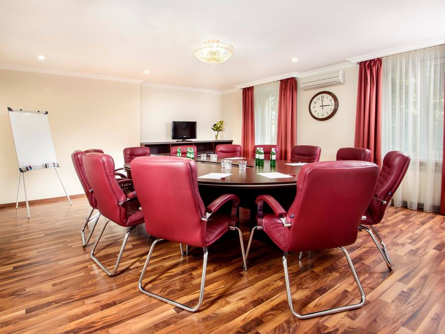 A conference room with a round table, red chairs, a whiteboard, a television, and a clock on the wall.