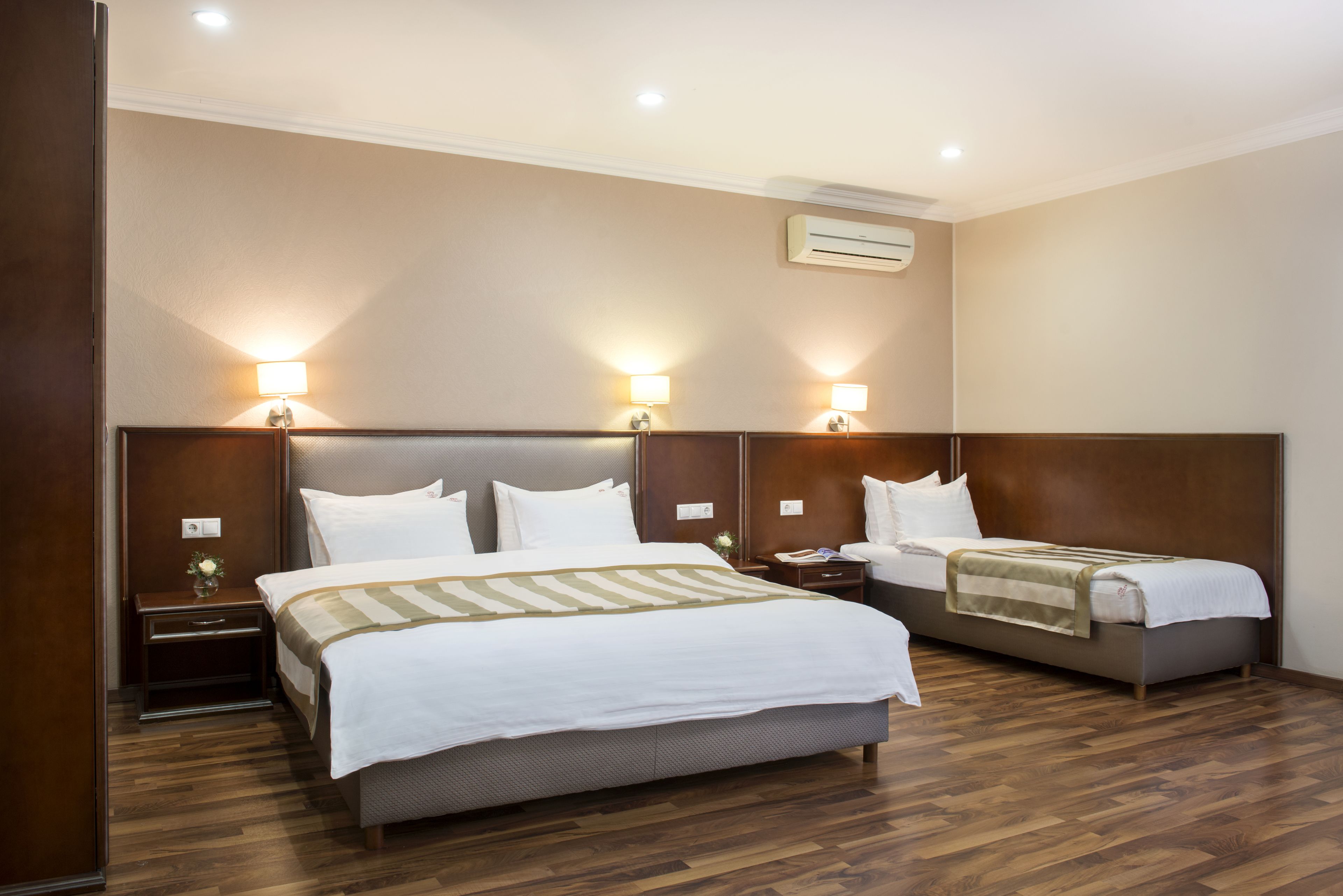 Ein Hotelzimmer mit einem großen Bett, einem kleineren Bett, Holzboden und Wandleuchten.