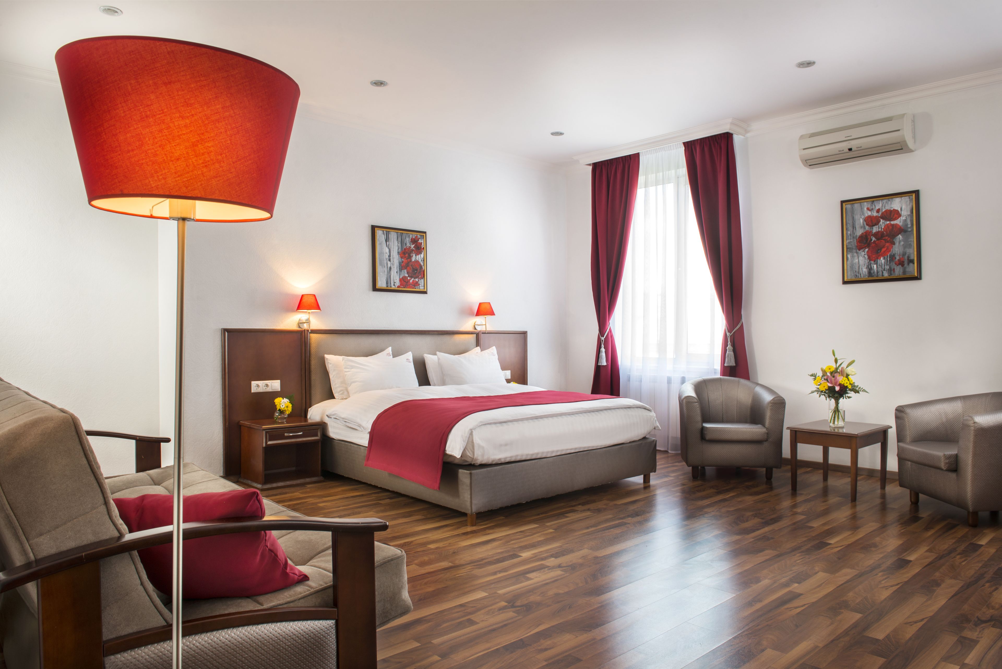 A hotel room with a bed, two chairs, a side table, a lamp, and a window with curtains.