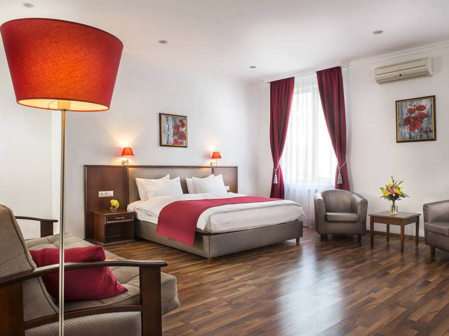 A hotel room with a bed, two chairs, a side table, a lamp, and a window with curtains.