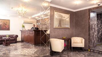 A lobby with a reception desk, a sofa, a chair, and a chandelier.