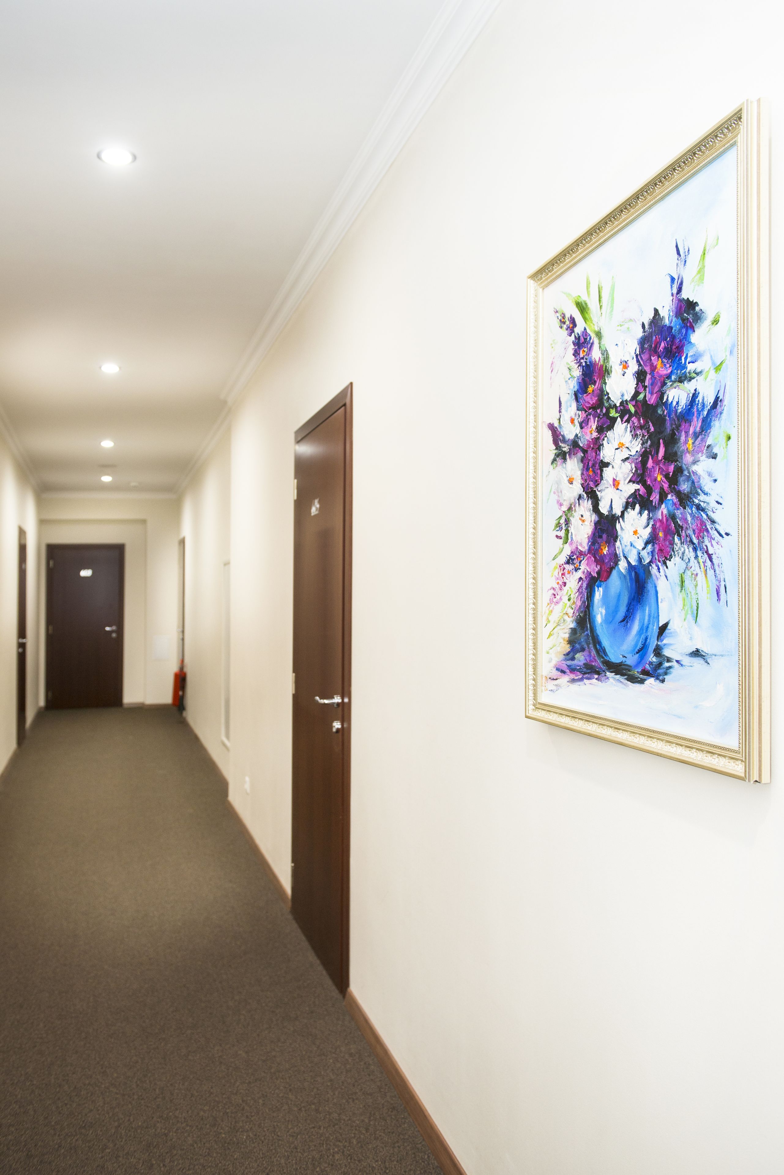 A hallway with a framed painting of flowers on the wall, a door, and a carpeted floor.