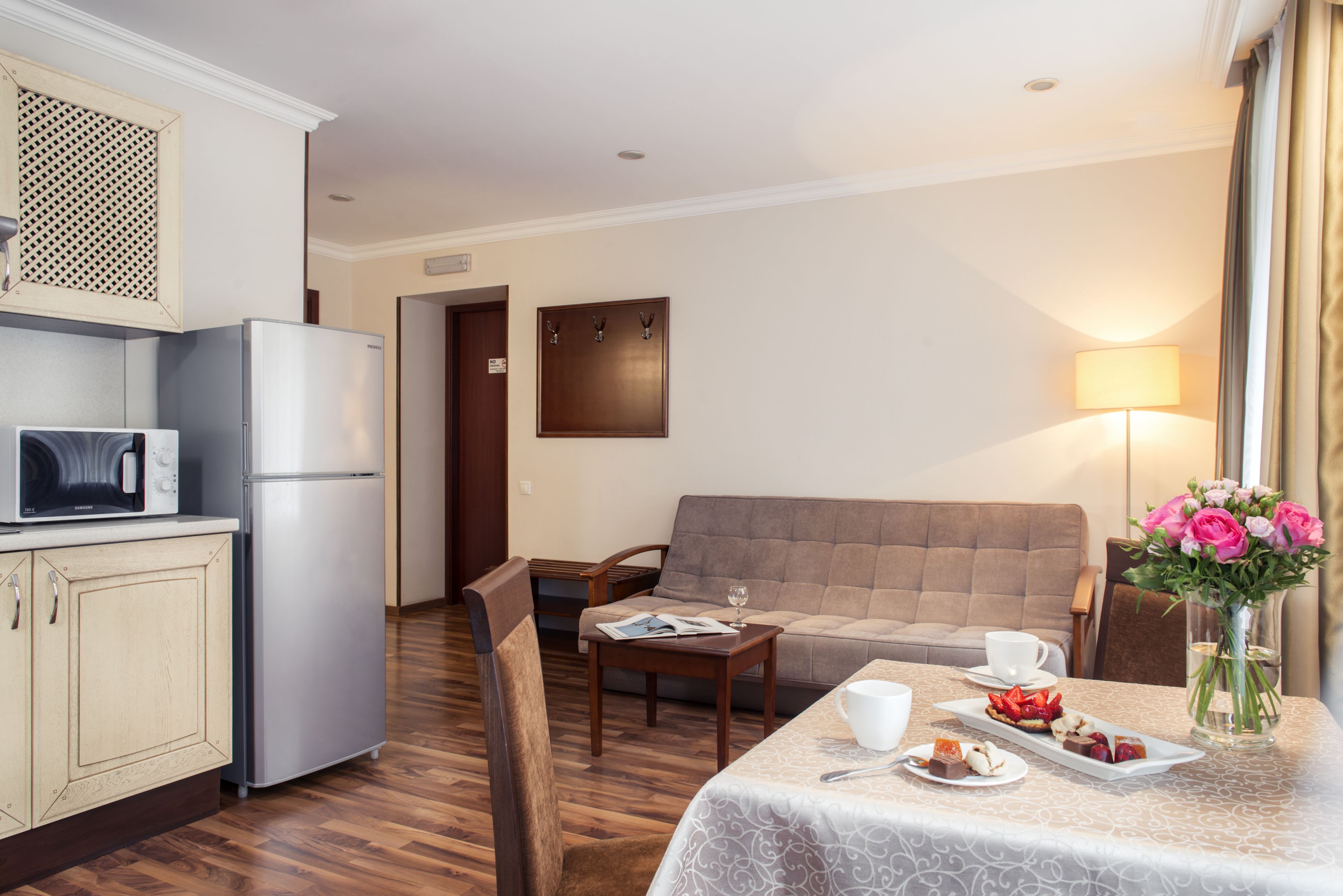 Ein Hotelzimmer mit Küchenzeile, einem Essbereich mit Tisch für zwei Personen, einer Couch und einer Lampe.
