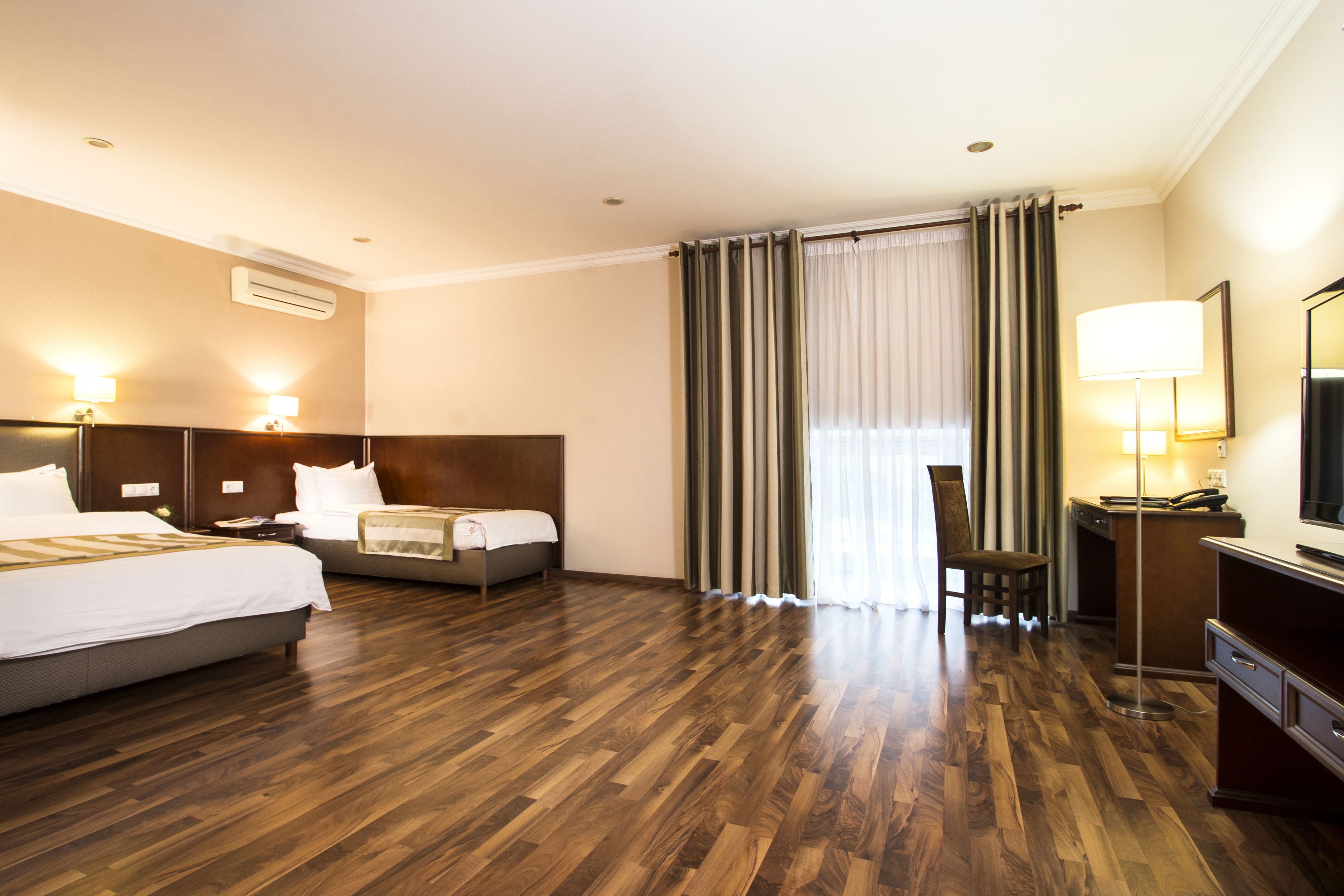A hotel room with two beds, a desk, a chair, and a large window with curtains.