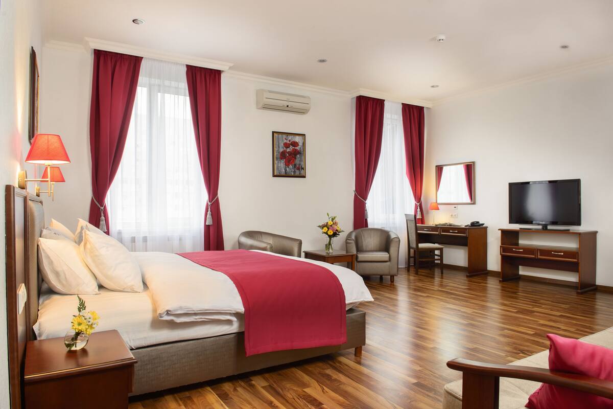 A hotel room with a bed, a desk, a chair, a TV, and a lamp.