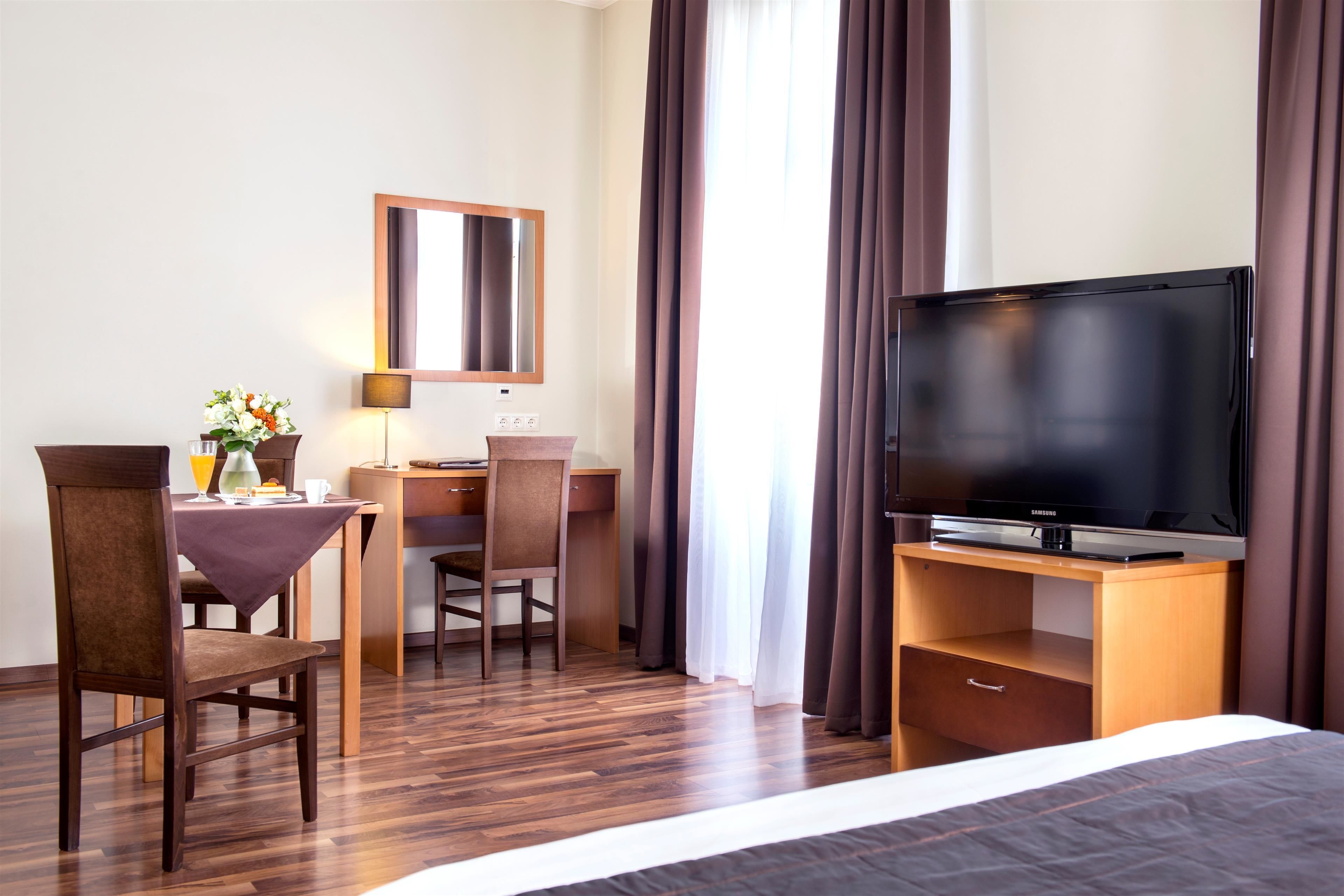 Une chambre d’hôtel comprenant un lit, un bureau avec une chaise, une télévision, une lampe et une fenêtre avec des rideaux.