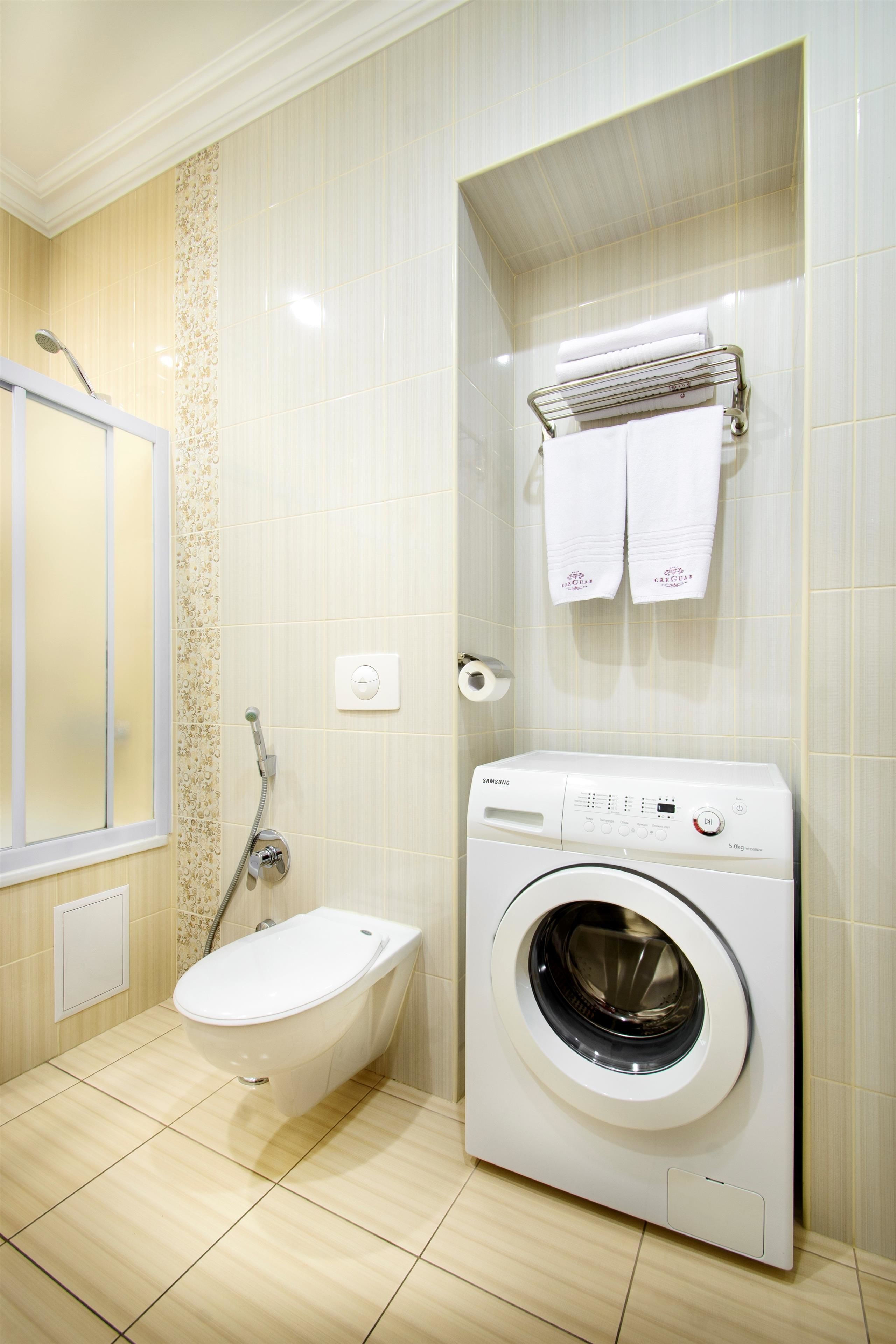 A compact bathroom with a toilet, a washing machine, and a towel rack.