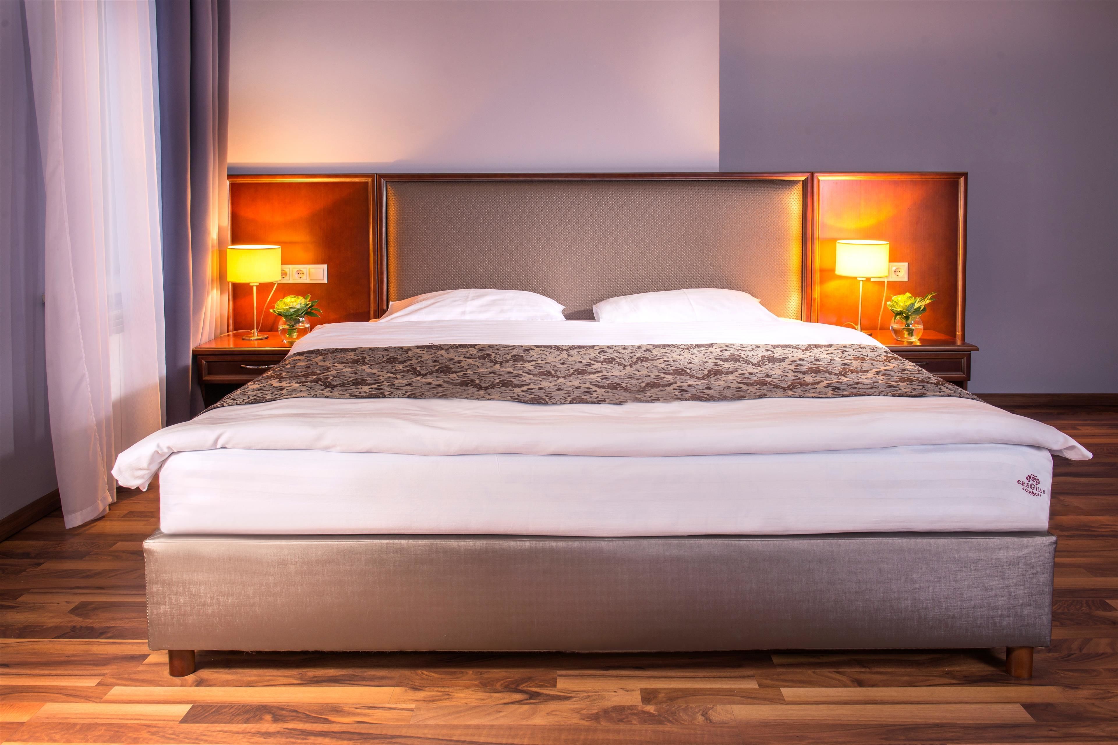 A neatly made bed with a headboard, two bedside tables with lamps, and a wooden floor.