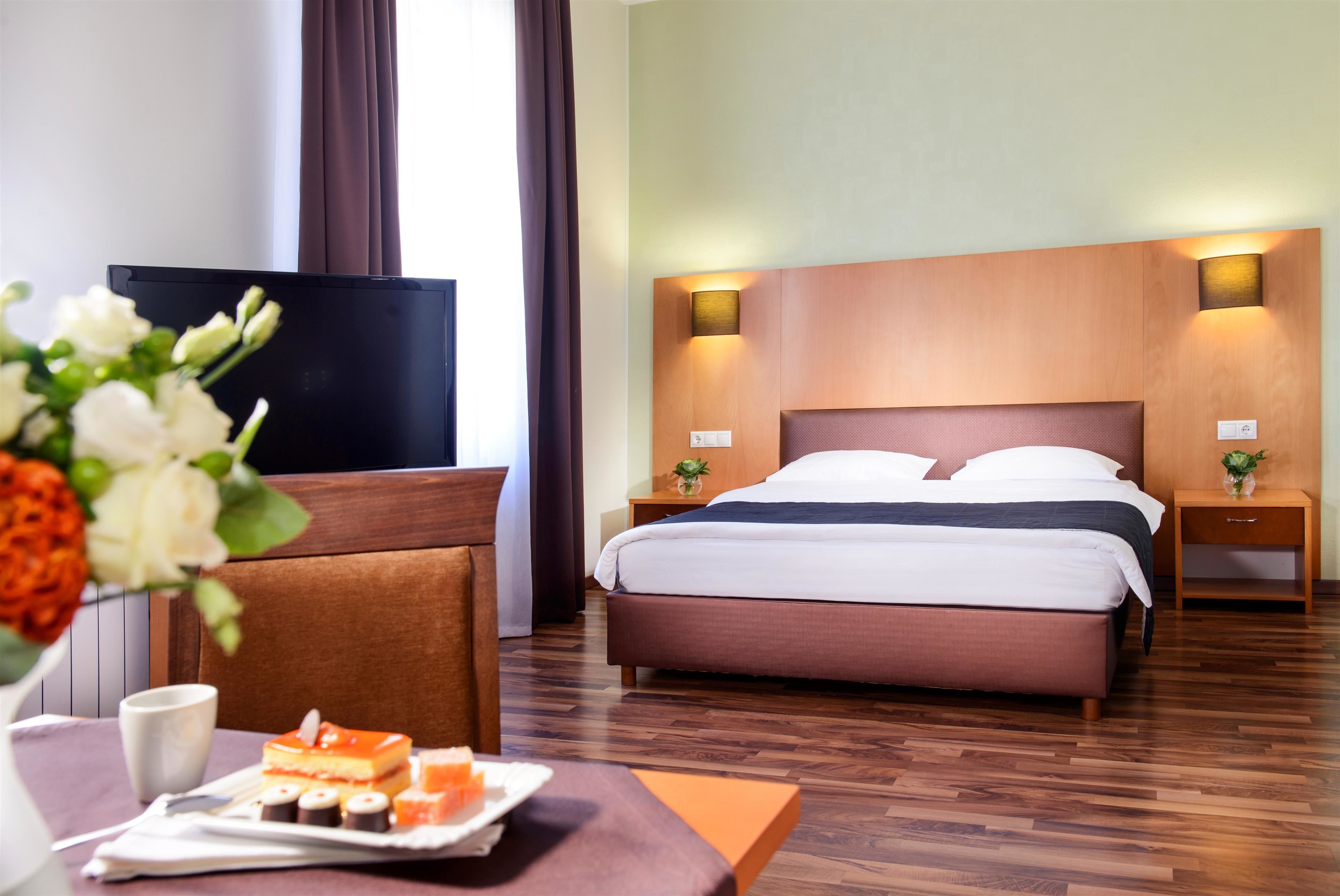 Una habitación de hotel con cama, mesitas de noche, televisor y una bandeja para el desayuno.