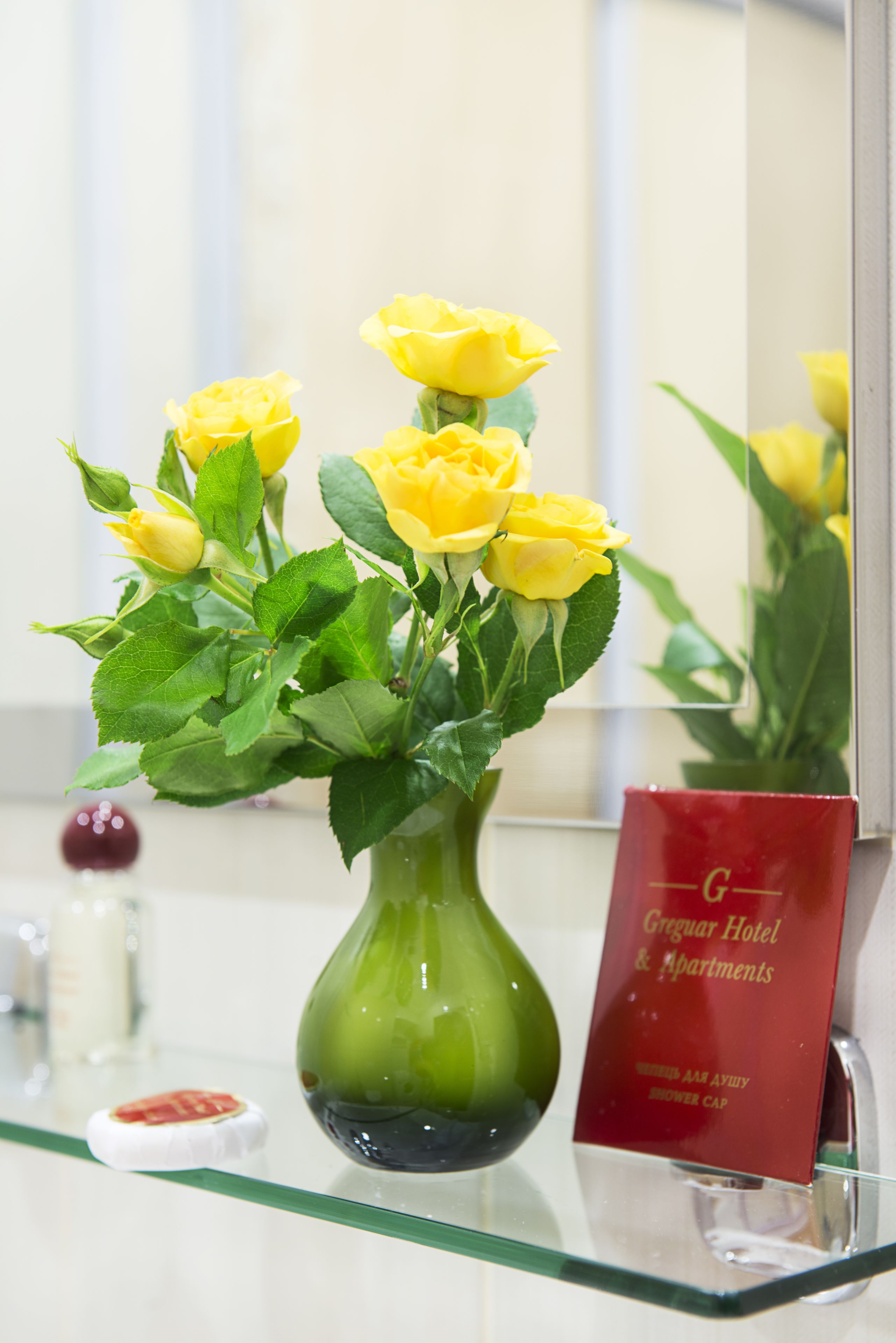 A green vase with yellow roses on a glass shelf.